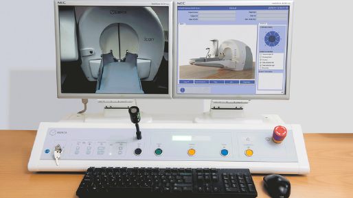 Photograph of two monitors showing a camera feed of an Elekta Leksell Gamma Knife icon and a dashboard with a control console in front